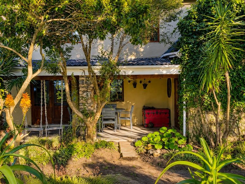 A charming covered patio area featuring stone detailing, timber-framed doors, and direct access to a lush, established garden setting.