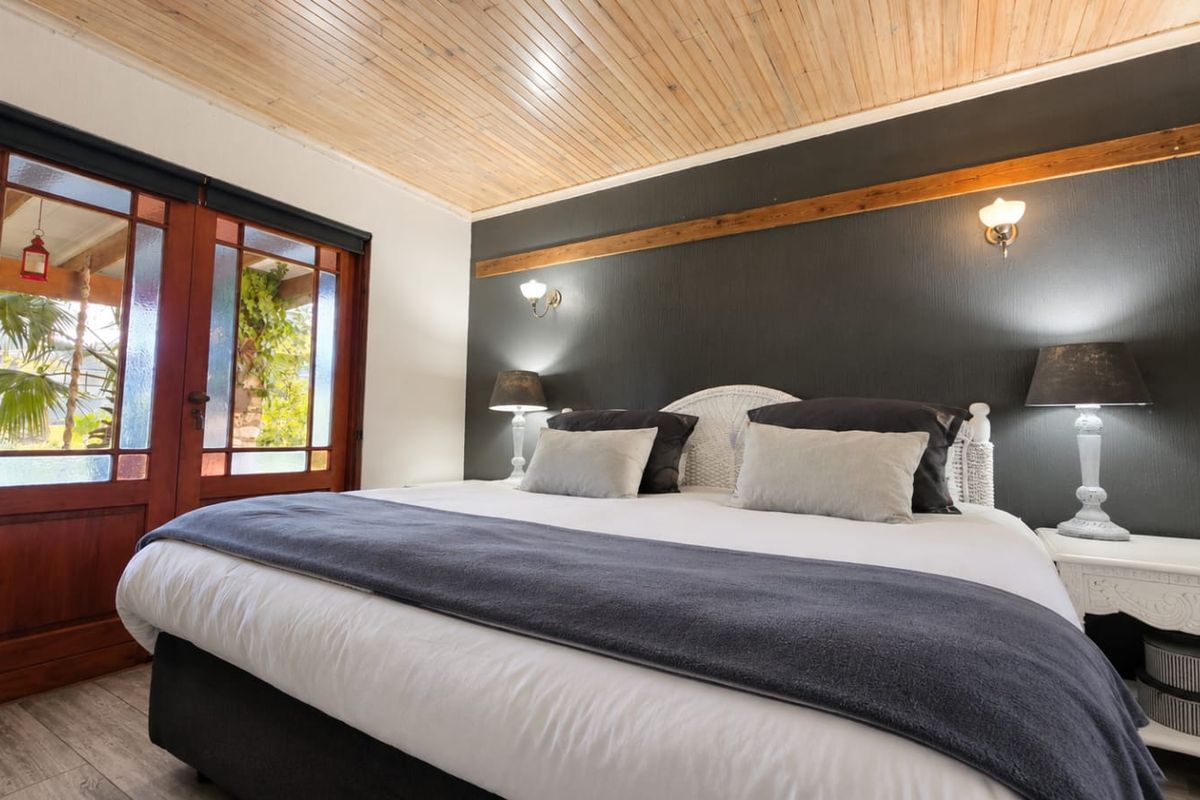 A well-maintained bedroom featuring a natural timber tongue and groove ceiling, dark accent wall, and timber-framed glass doors providing access to the outdoors.