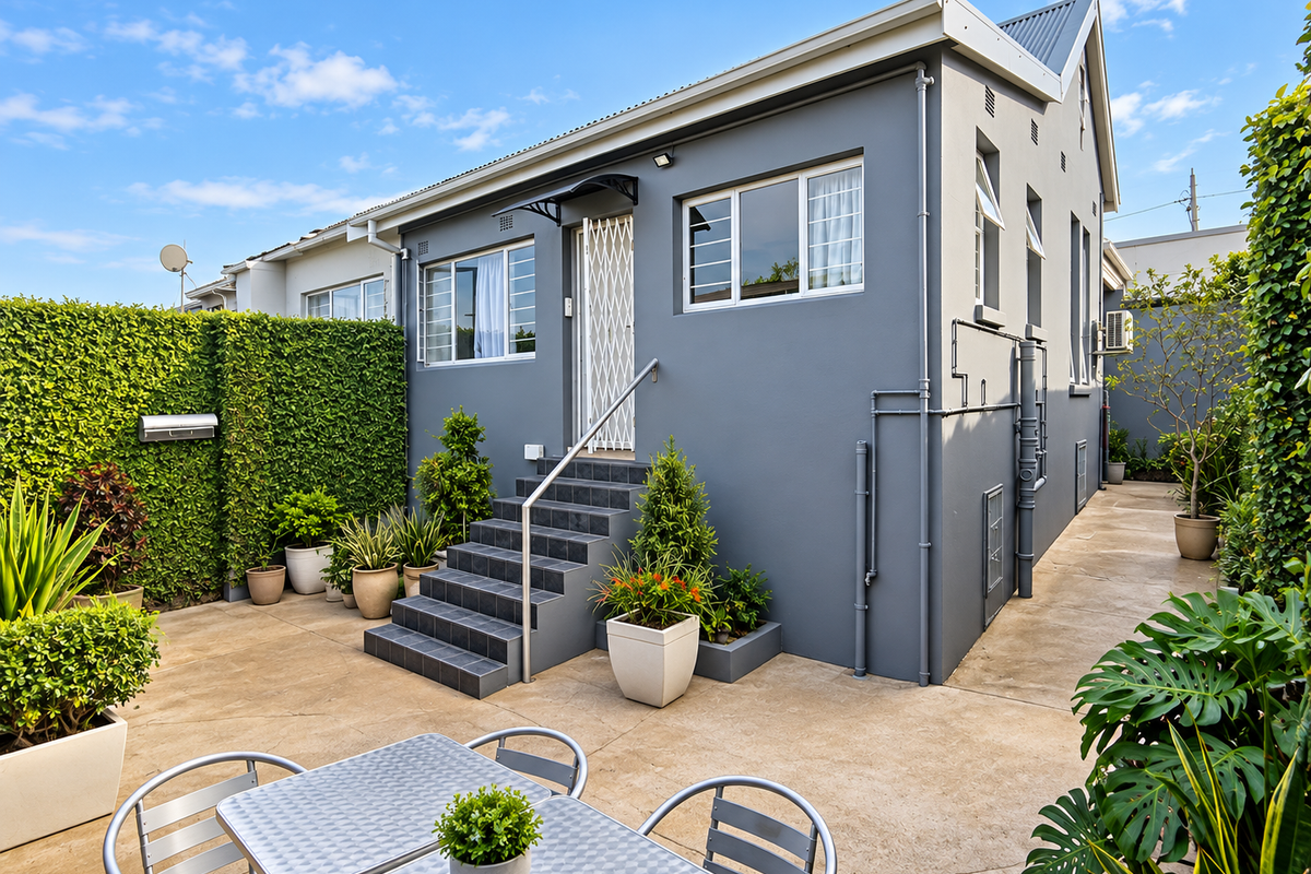 Well-maintained rear exterior of a townhouse featuring a tiled staircase, secure entrance, and a paved patio area surrounded by established greenery.