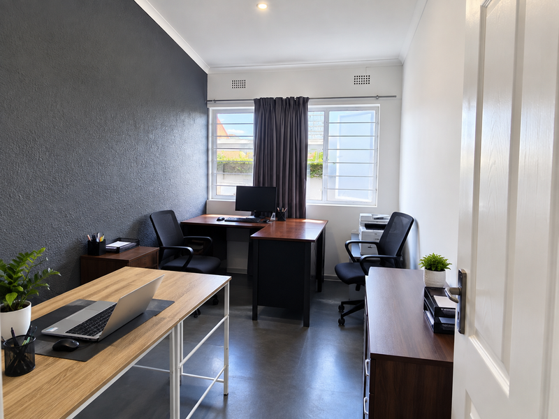 A well-lit home office featuring a dark textured accent wall, tiled flooring, and large horizontal sliding windows providing natural light.