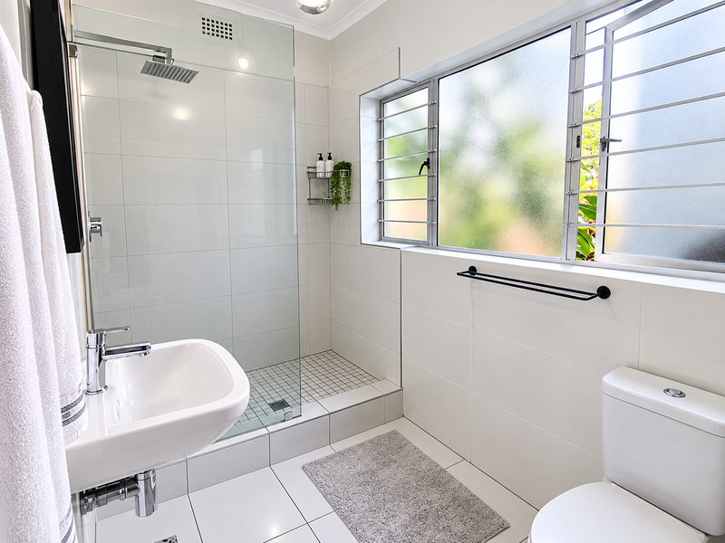 Modern bathroom featuring a walk-in shower with glass screen, rain shower head, wall-mounted basin, and tiled finishes throughout.