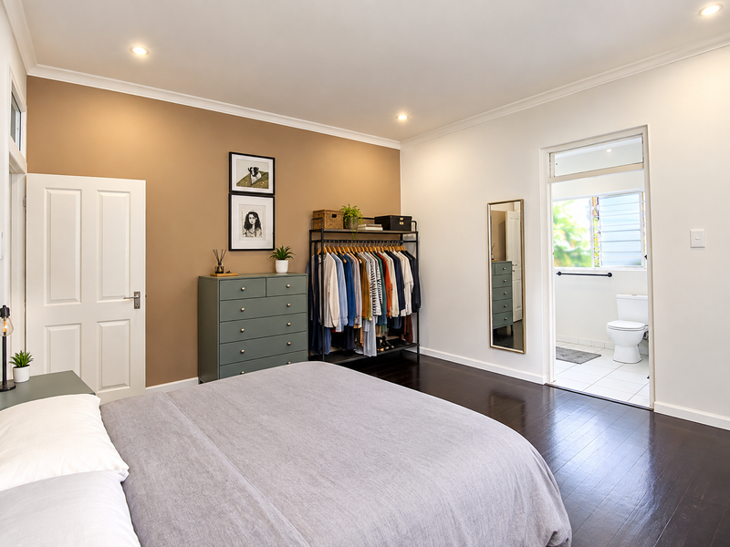 Spacious bedroom featuring dark timber flooring, recessed downlighting, and an adjoining en-suite bathroom with louver windows.