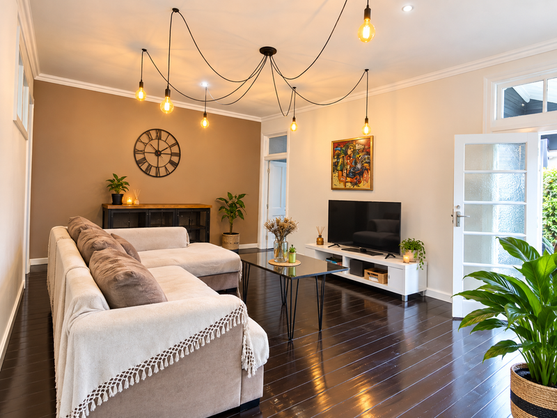 A well-maintained living room featuring dark stained timber flooring, a modern spider pendant light fixture, and a glass-paneled french door leading outdoors.