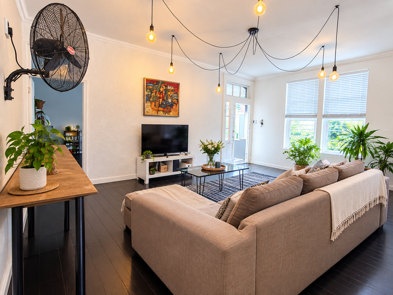 A bright and well-maintained living room featuring dark hardwood floors, textured walls, and modern multi-pendant lighting with access to an outdoor area.
