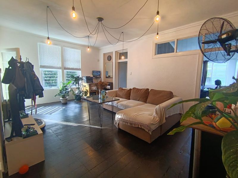 A spacious living room featuring dark timber flooring, large windows with venetian blinds, and decorative coving, offering a bright and characterful living space.