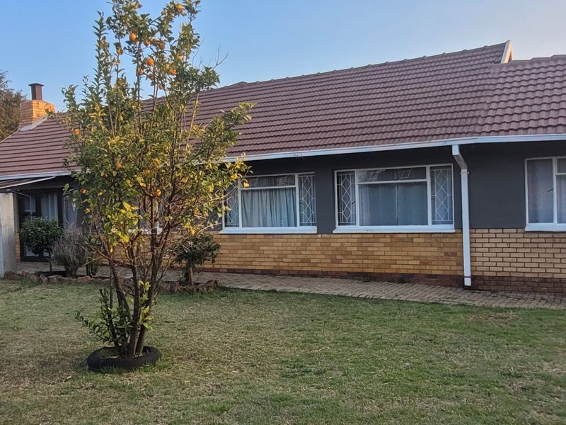 Rear view of a single-story residential house featuring a tiled roof, brick and painted exterior walls, and a paved walkway leading to the garden.