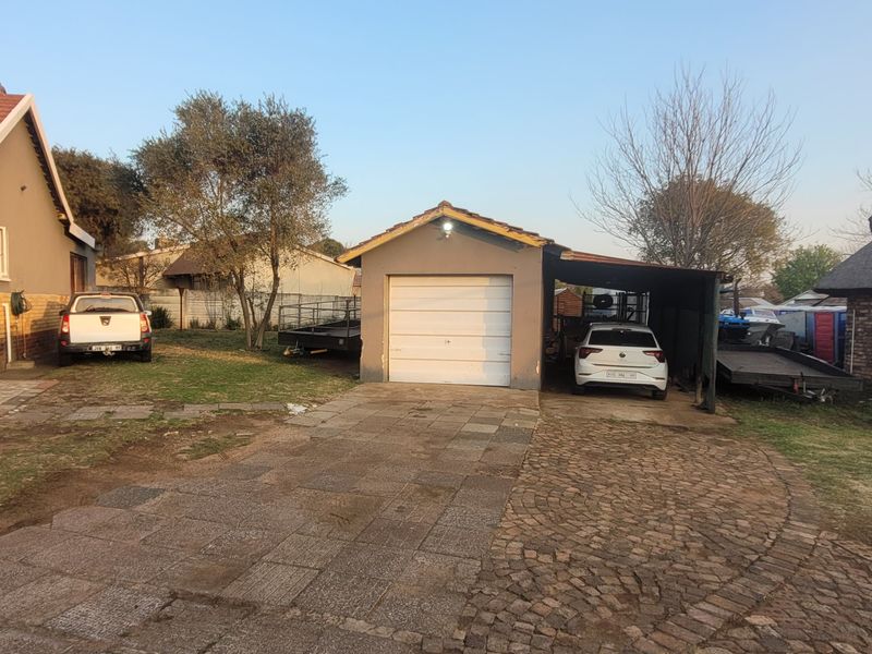 Rear exterior view featuring a single garage, attached carport, paved driveway, and a mix of brick and thatched roof structures.