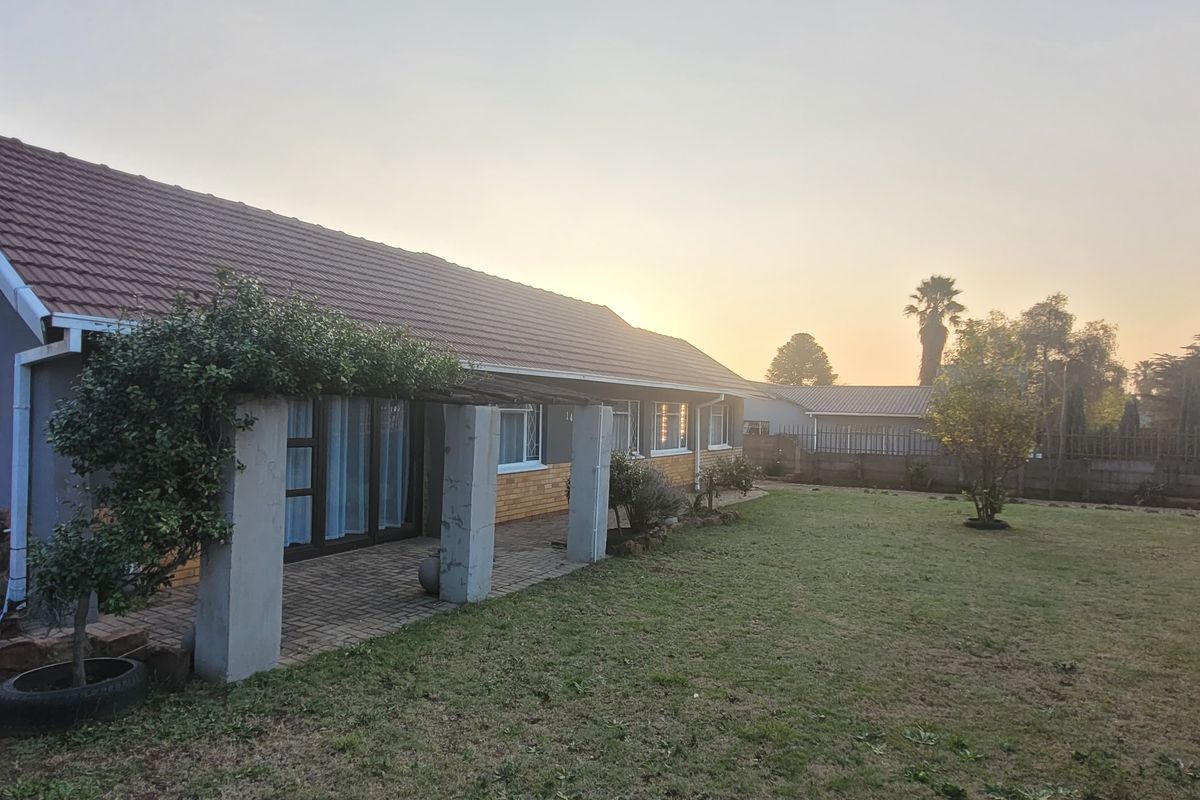 Rear view of the house featuring a tiled roof, brick chimney, and a covered patio area overlooking the garden.