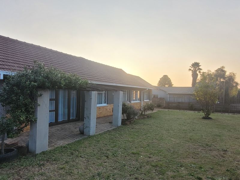 Rear view of the house featuring a tiled roof, brick chimney, and a covered patio area overlooking the garden.