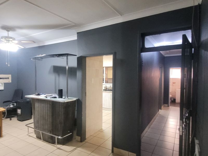 A living area featuring dark painted walls, tiled flooring, a ceiling fan, and a built-in bar, with access to a hallway and kitchen.