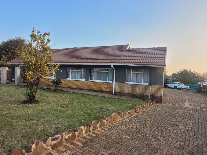 Front view of a single-story house featuring a tiled roof, brick and painted facade, and a spacious paved driveway with a landscaped front garden.
