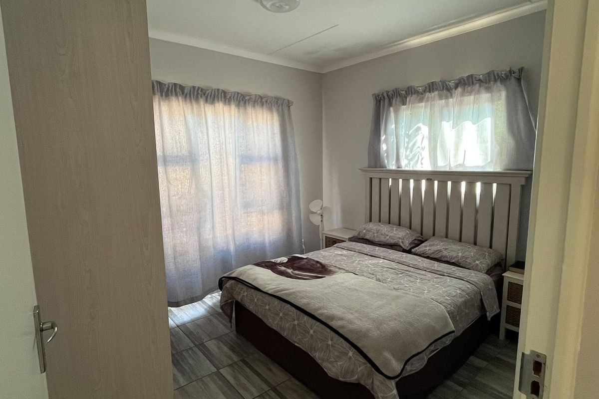 A functional bedroom featuring tiled flooring and natural light through dual windows, providing a neutral base for personal styling.