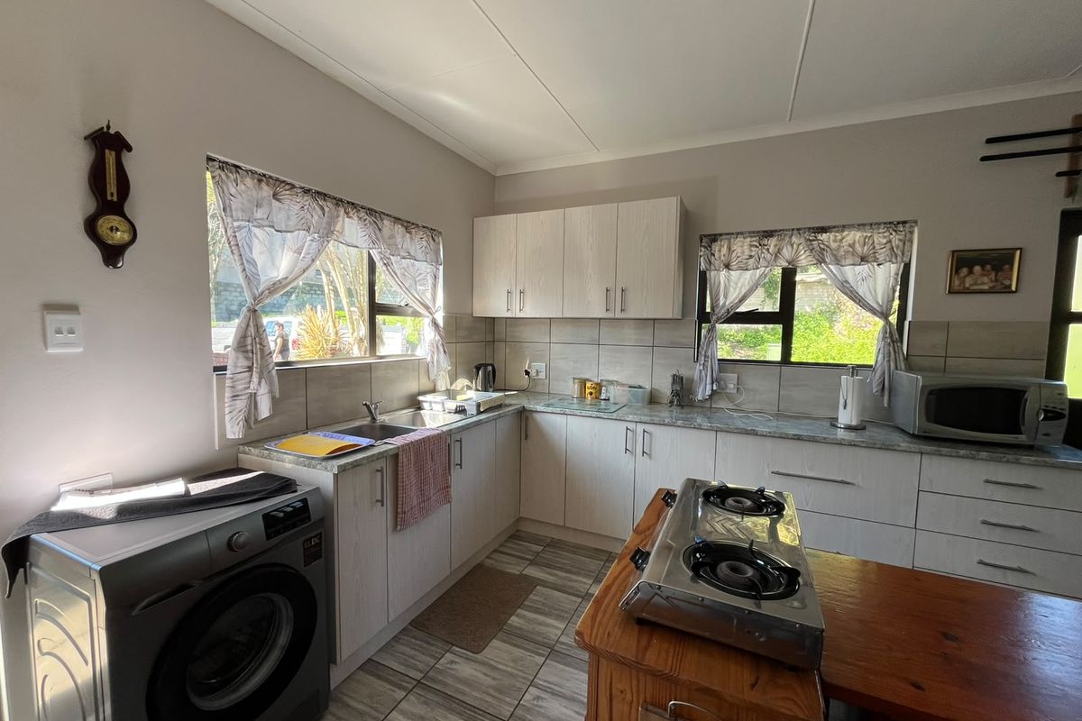 A functional kitchen featuring light-toned built-in cabinetry, laminate countertops, tiled backsplash, and tiled flooring with ample natural light from dual windows.
