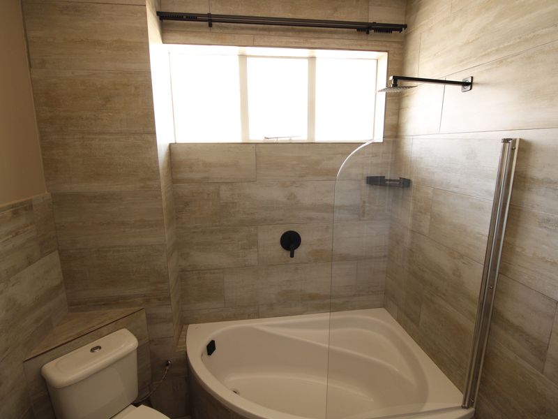 Modern bathroom featuring neutral-toned wall tiles, a corner bathtub with a glass shower screen, and contemporary black fixtures.