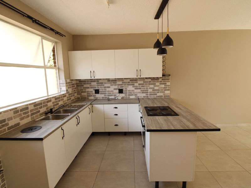 Modern kitchen featuring white cabinetry, wood-look laminate countertops, a built-in hob and oven, tiled backsplash, and neutral floor tiles.