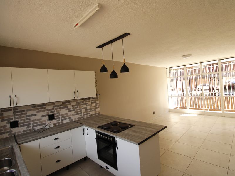 Modern open-plan kitchen featuring white cabinetry, wood-look countertops, built-in appliances, and tiled flooring, flowing into a bright living area with large sliding doors.