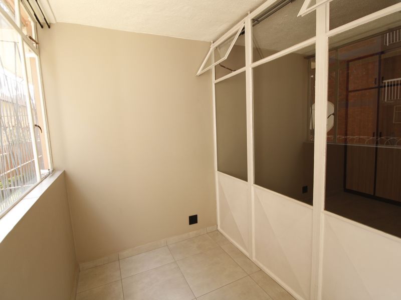 An enclosed balcony or sunroom featuring tiled flooring, white aluminium window frames, and a glass partition wall, offering a bright and versatile space.