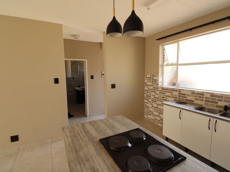 A clean, functional kitchen featuring a central island with a built-in hob, modern cabinetry, tiled backsplash, and neutral finishes throughout.