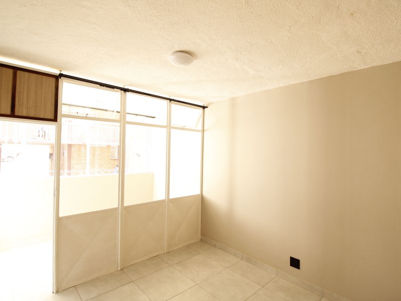 An empty bedroom featuring tiled flooring, a built-in cupboard, and a glass partition wall leading to an adjacent space.
