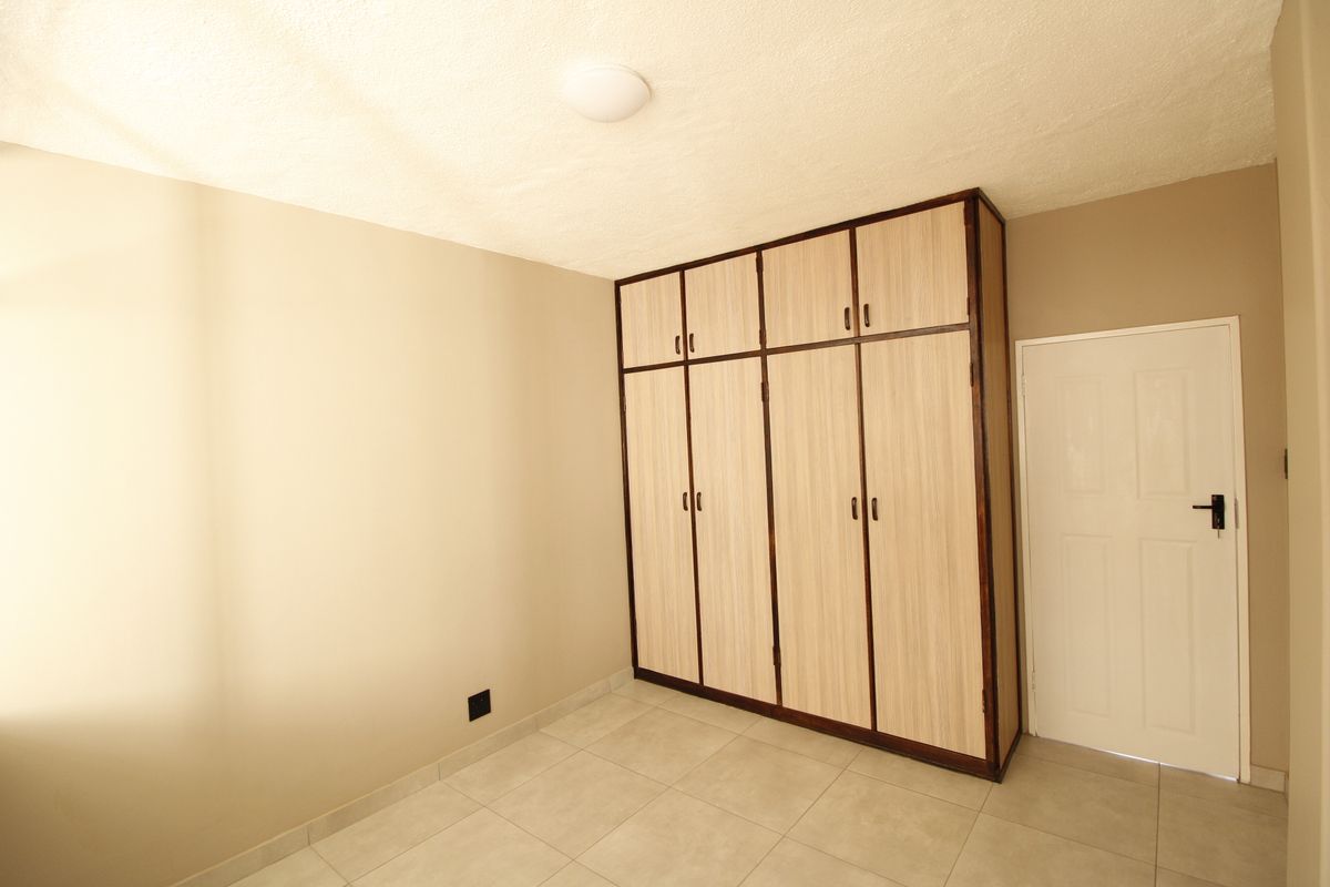 A clean, empty bedroom featuring neutral wall tones, light-colored tiled flooring, and ample built-in cupboard storage space.