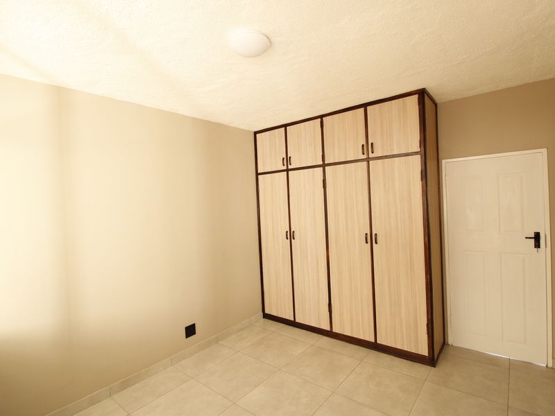 A clean, empty bedroom featuring neutral wall tones, light-colored tiled flooring, and ample built-in cupboard storage space.