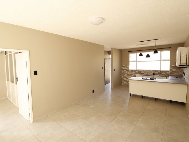 Spacious open-plan living and kitchen area featuring neutral tiled flooring, a functional kitchen island with a built-in hob, and modern pendant lighting.