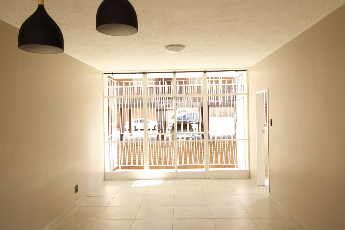 An empty, neutrally painted living area featuring tiled flooring and large glass panels with an integrated security gate.