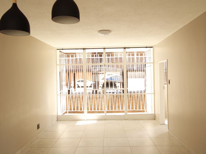An empty, neutrally painted living area featuring tiled flooring and large glass panels with an integrated security gate.