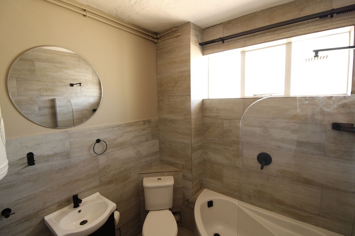A modern bathroom featuring wood-look wall tiles, a bathtub with a glass screen, a wall-mounted basin, and a toilet.