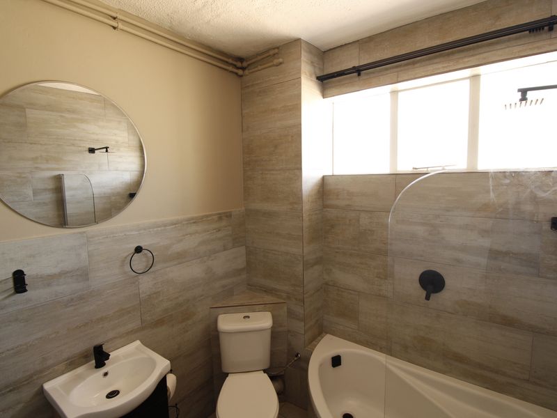 A modern bathroom featuring wood-look wall tiles, a bathtub with a glass screen, a wall-mounted basin, and a toilet.