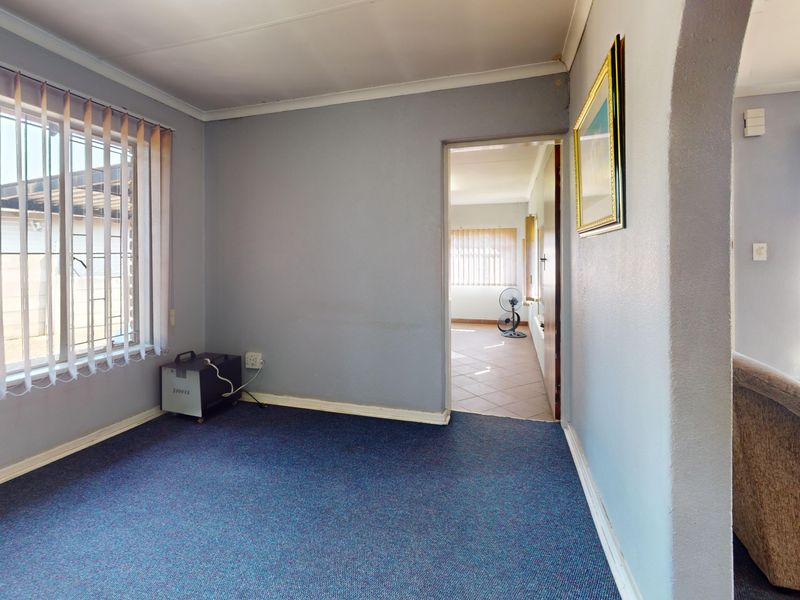 A neutrally painted living area featuring carpeted flooring, vertical blinds, and an arched entryway leading to an adjacent tiled room.