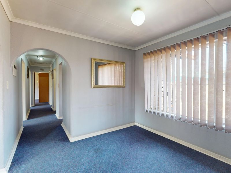 An empty living room featuring an arched entryway, brick accent wall, and large window with vertical blinds, leading into a central hallway.