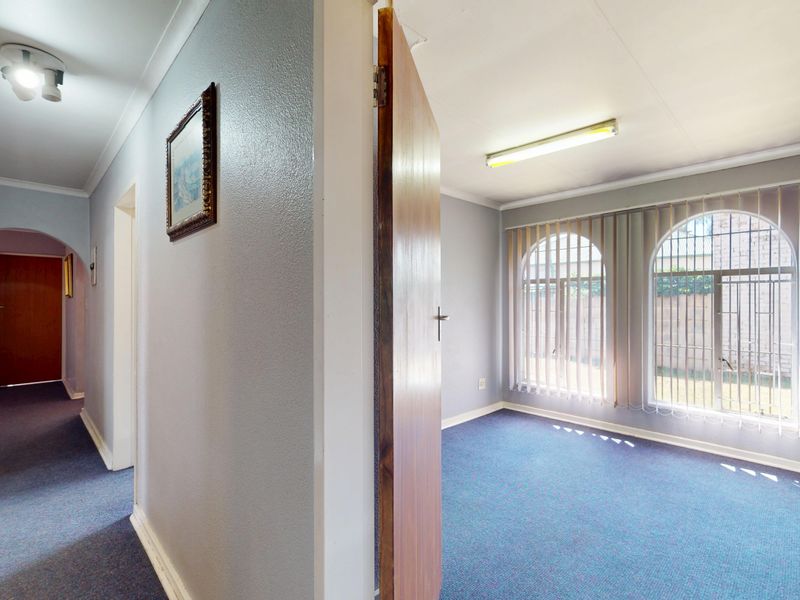 A view from a hallway looking into an empty bedroom featuring arched windows with security bars and vertical blinds.