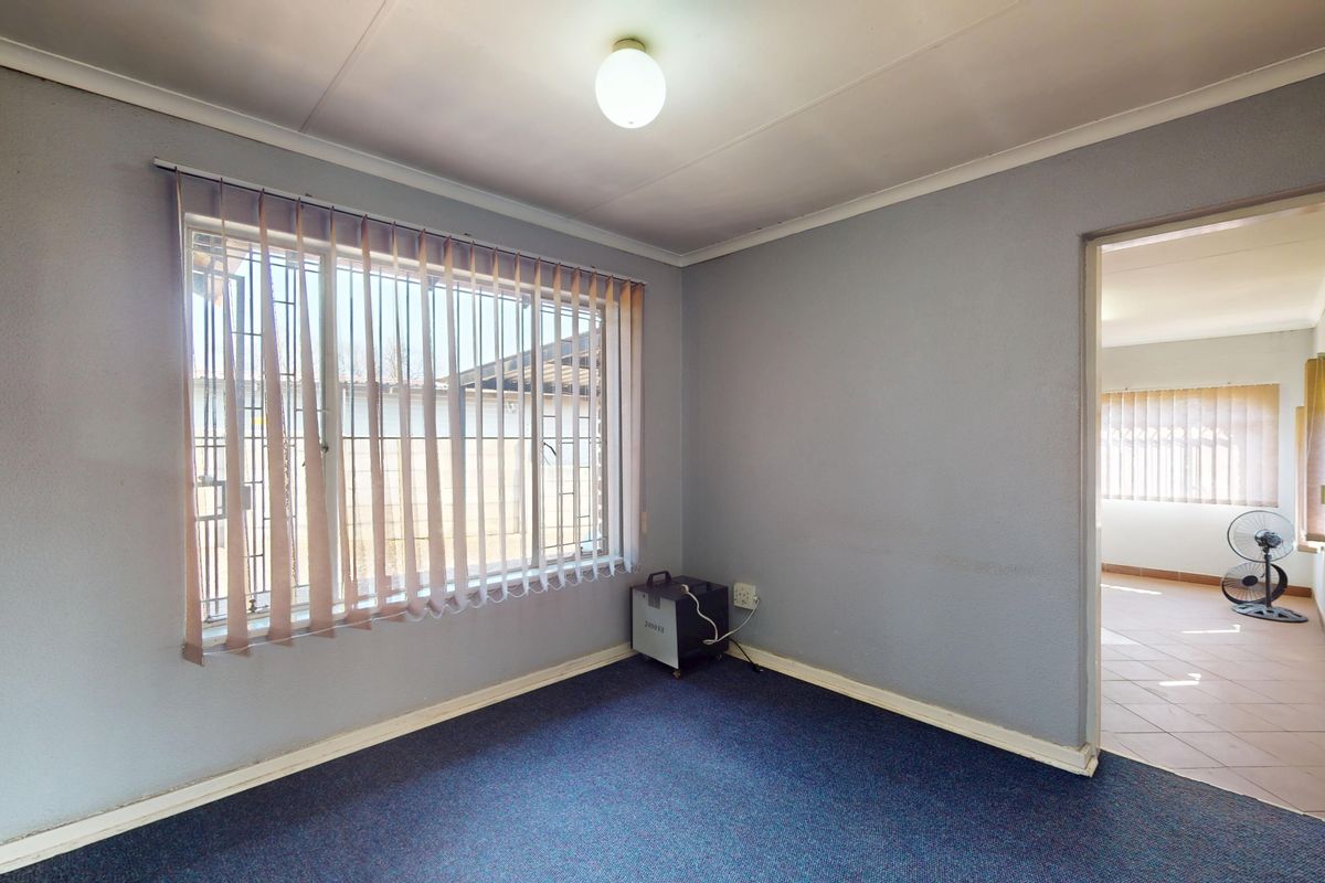 An empty bedroom featuring carpet flooring, vertical blinds, and security bars on the window, offering a blank canvas for potential updates.