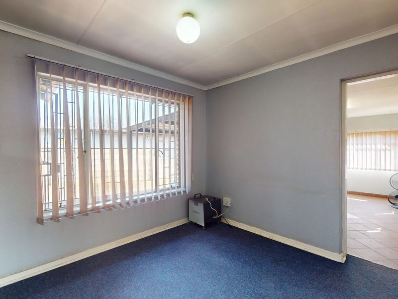 An empty bedroom featuring carpet flooring, vertical blinds, and security bars on the window, offering a blank canvas for potential updates.