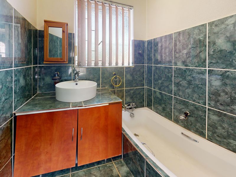 A functional bathroom featuring a built-in vanity with a vessel sink, a bathtub, and full-height green marble-effect wall tiling.