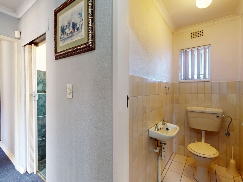 A compact, dated bathroom featuring a wall-mounted basin and standard toilet with neutral ceramic tiling throughout.