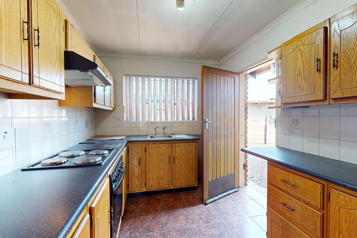 A functional kitchen featuring wood-finish cabinetry, dark laminate countertops, built-in oven and hob, and direct access to the exterior.