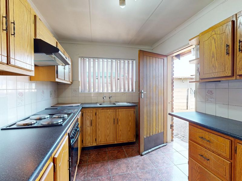 A functional kitchen featuring wood-finish cabinetry, dark laminate countertops, built-in oven and hob, and direct access to the exterior.