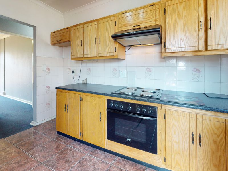 A functional kitchen featuring traditional wooden cabinetry, a dark laminate countertop, built-in oven with hob, and a tiled backsplash.
