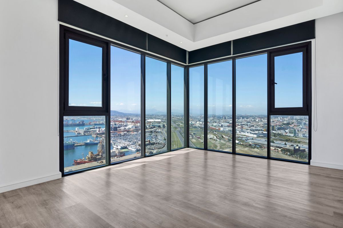 A bright, empty living area featuring expansive floor-to-ceiling corner windows with panoramic harbor and city views, finished with modern laminate flooring.
