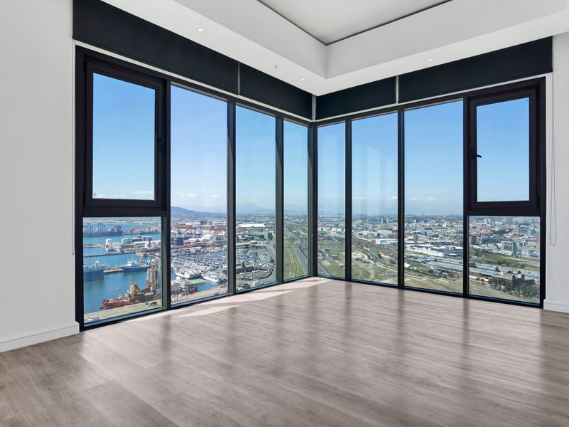 A bright, empty living area featuring expansive floor-to-ceiling corner windows with panoramic harbor and city views, finished with modern laminate flooring.