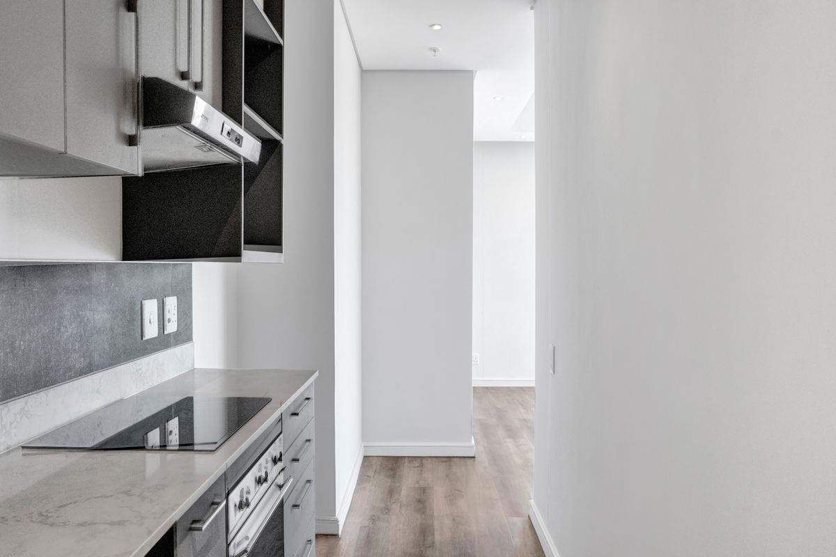 Modern kitchen featuring sleek grey cabinetry, stone countertops, integrated electric hob and oven, and recessed lighting, leading into an open-plan living area.