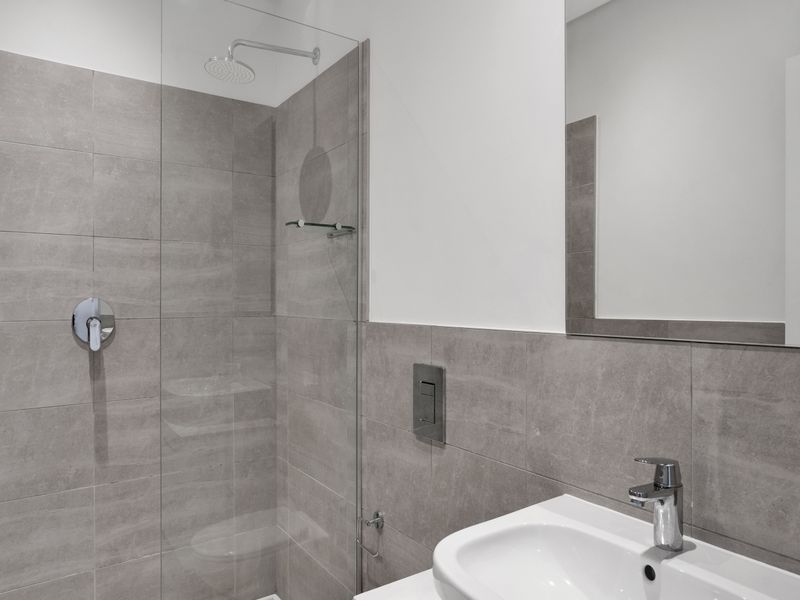 Modern bathroom featuring a walk-in shower with glass screen, rain shower head, wall-hung toilet flush plate, and a sleek vanity basin with mirror.