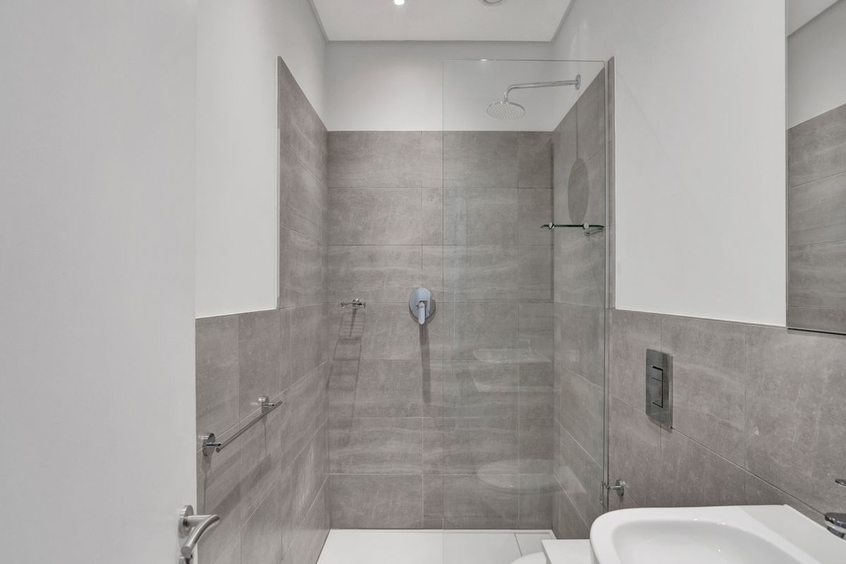 Modern bathroom featuring a walk-in shower with a glass screen, rain shower head, and contemporary grey tiling.