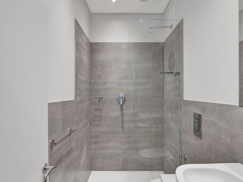 Modern bathroom featuring a walk-in shower with a glass screen, rain shower head, and contemporary grey tiling.