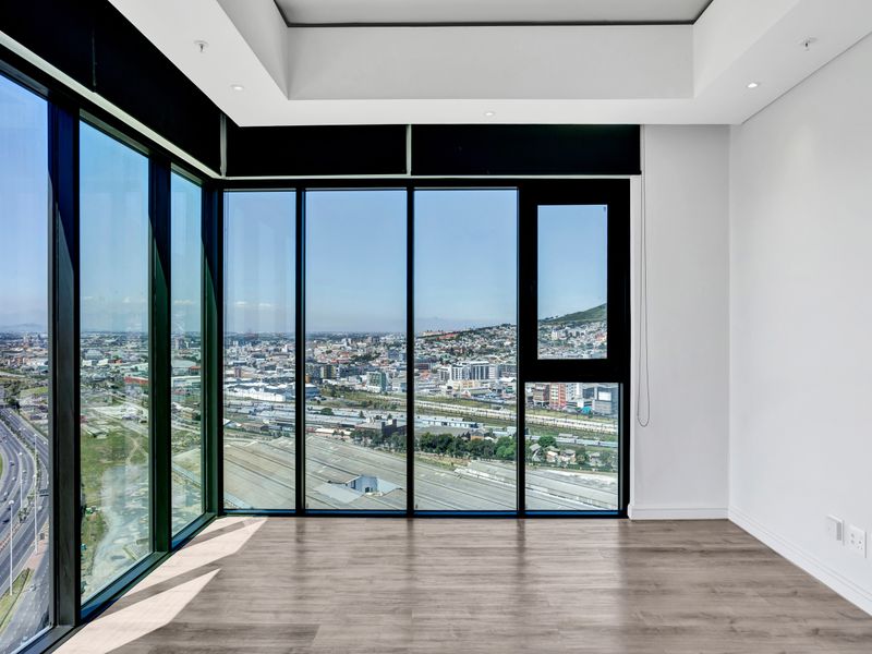 Bright and modern living area featuring expansive floor-to-ceiling windows with panoramic city views, neutral finishes, and high-quality laminate flooring.