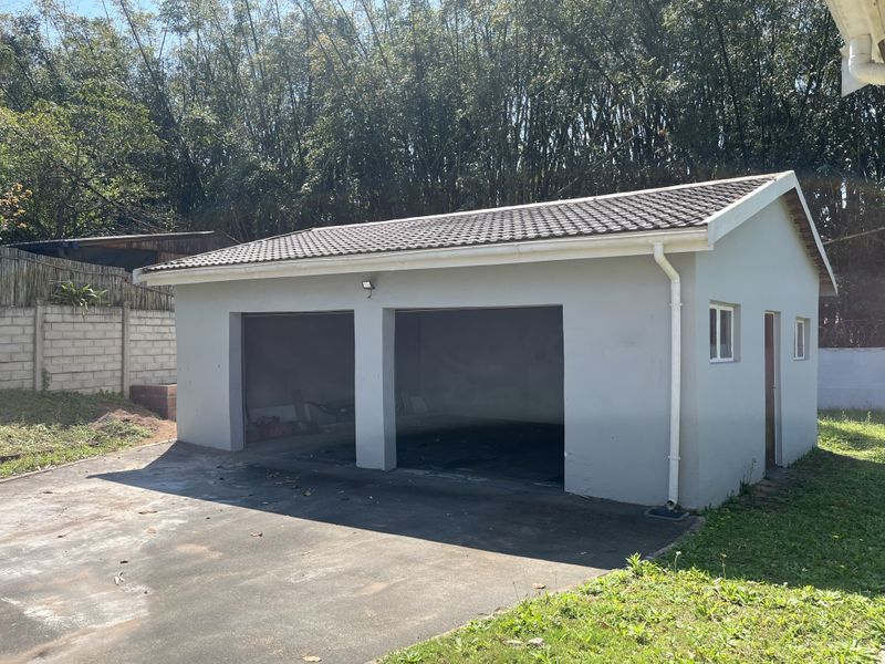 A detached double garage featuring a tiled roof, exterior lighting, and a concrete driveway, set within a garden area.