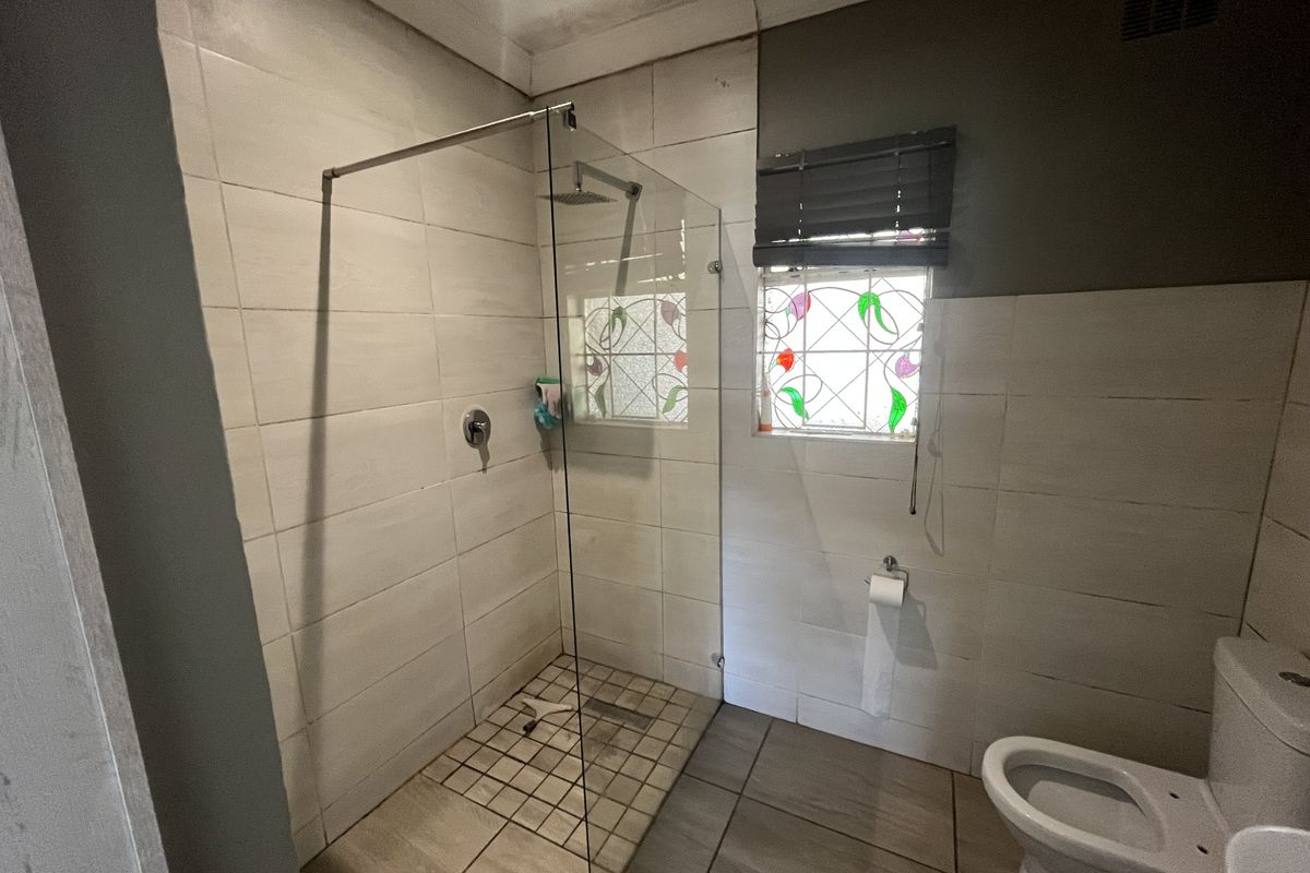 A functional bathroom featuring a walk-in glass shower, tiled finishes, and a decorative stained glass window.