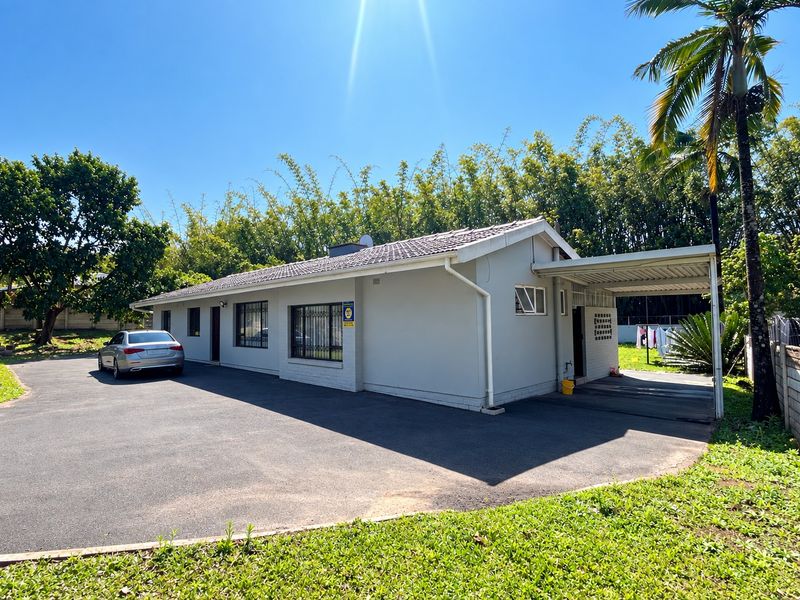 A well-maintained single-story house featuring a tiled roof, a paved driveway, and an attached carport, set within a landscaped garden.